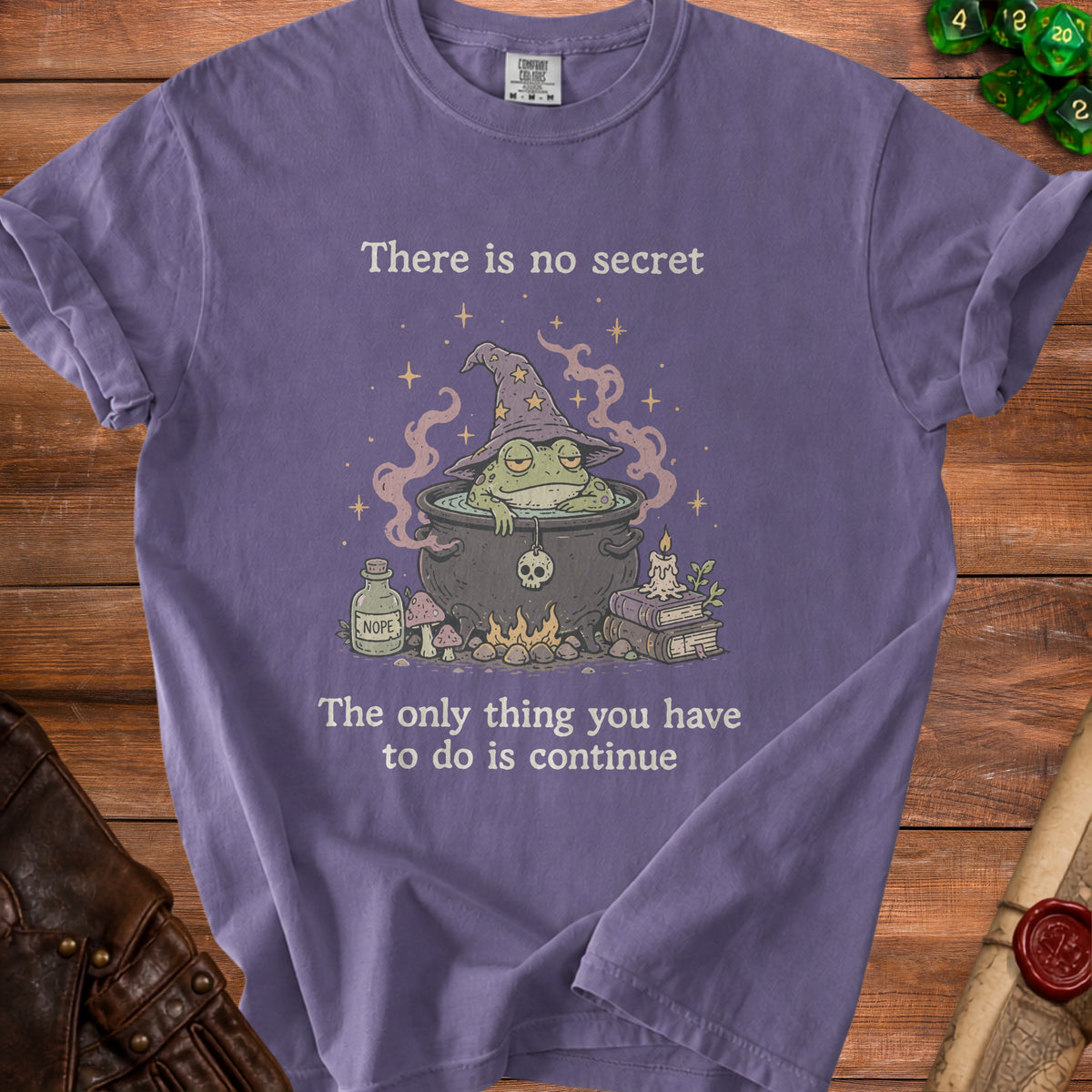 Purple t-shirt with a witch frog in a cauldron and the text "There is no secret" and "The only thing you have to do is continue".