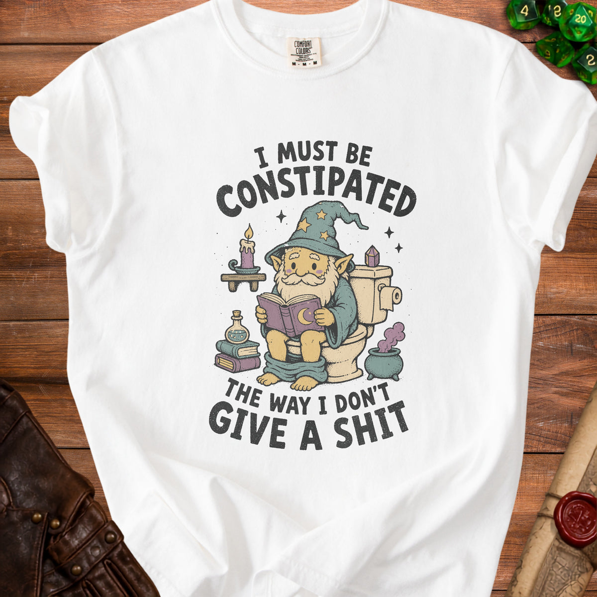 White t-shirt with graphic of wizard on toilet reading and text "I MUST BE CONSTIPATED THE WAY I DON'T GIVE A SHIT".