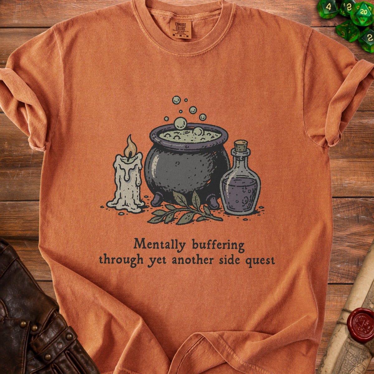 Orange t-shirt with a cauldron, candle, potion, and text "Mentally buffering through yet another side quest".