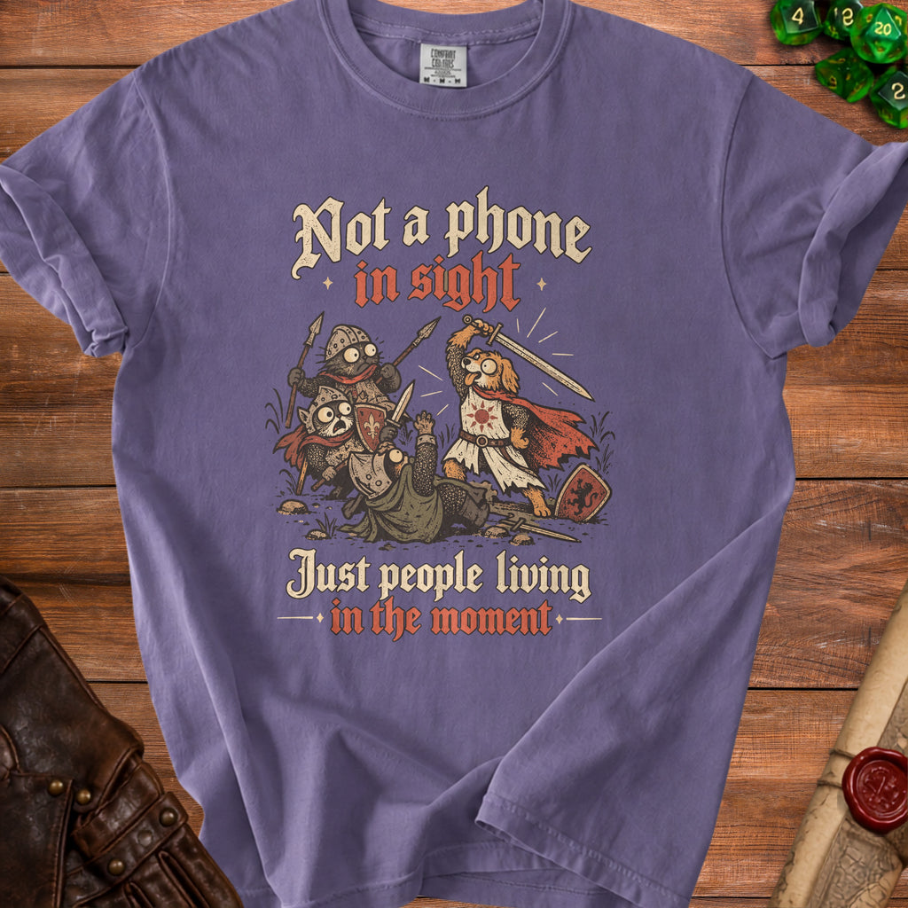 Purple t-shirt with cartoon cats and dog knights fighting, text "Not a phone in sight. Just people living in the moment."