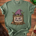 A green t-shirt featuring a graphic of a creature in a tree stump wearing a witch hat and a sign that reads DO NOT PERCEIVE.