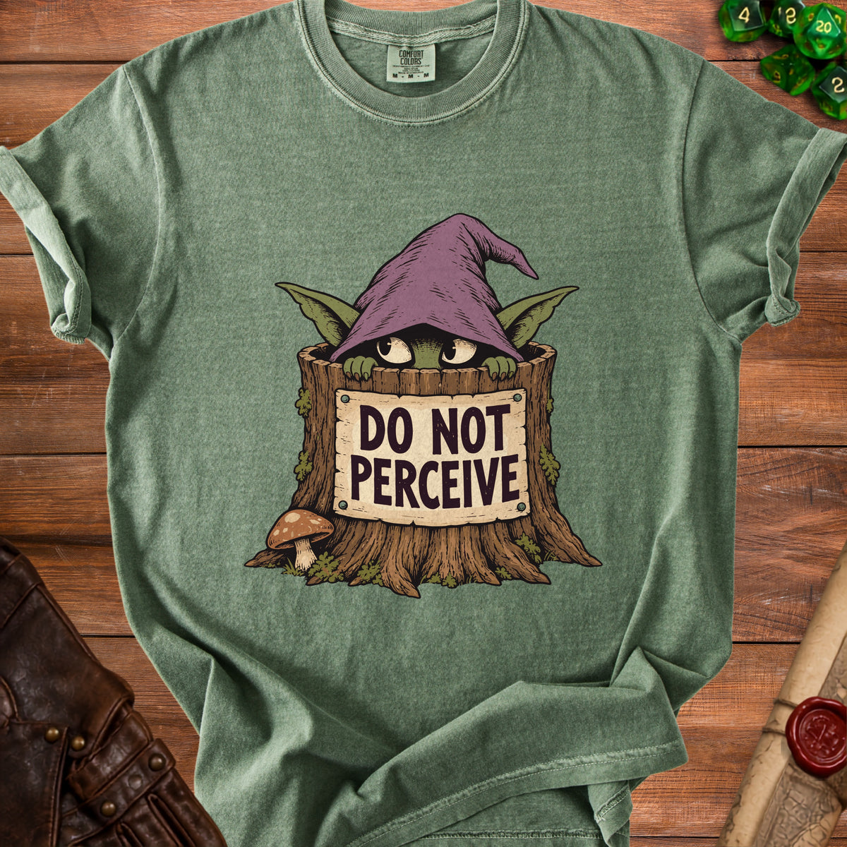 A green t-shirt featuring a graphic of a creature in a tree stump wearing a witch hat and a sign that reads DO NOT PERCEIVE.