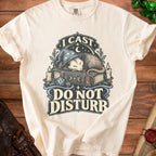 Off-white t-shirt featuring a sleeping opossum in a wizard hat on a book with the text I Cast Do Not Disturb.
