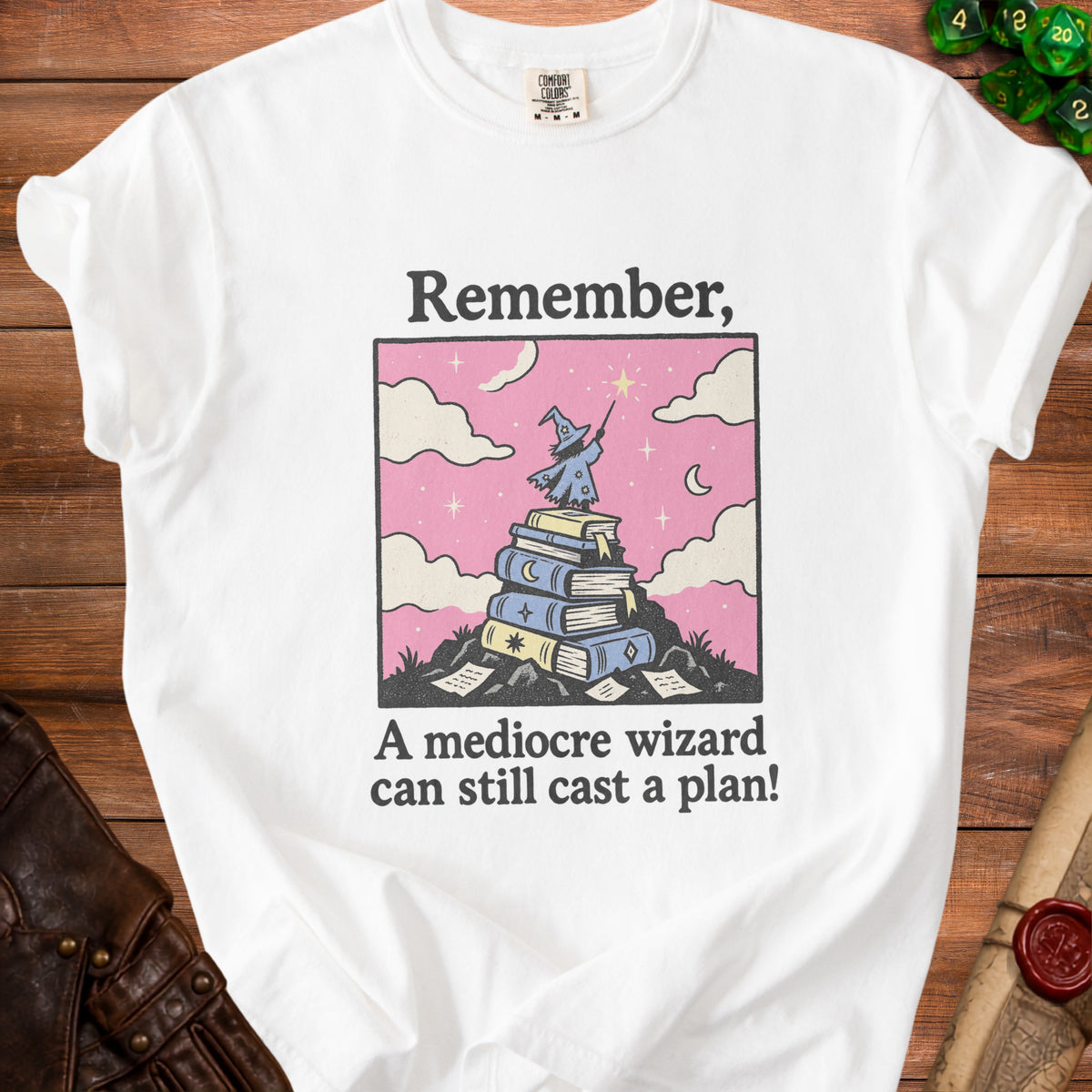 A white t-shirt featuring a wizard standing on books with text reading Remember, A mediocre wizard can still cast a plan!