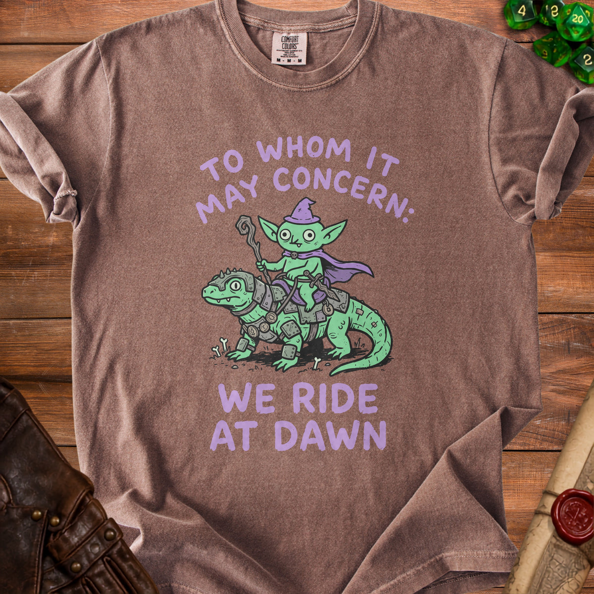 Brown t-shirt with a goblin riding a dinosaur and text "WE RIDE AT DAWN".