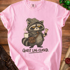 Pink t-shirt with raccoon character in medieval garb holding coffee and scroll, text "QUEST LOG CLOSED."