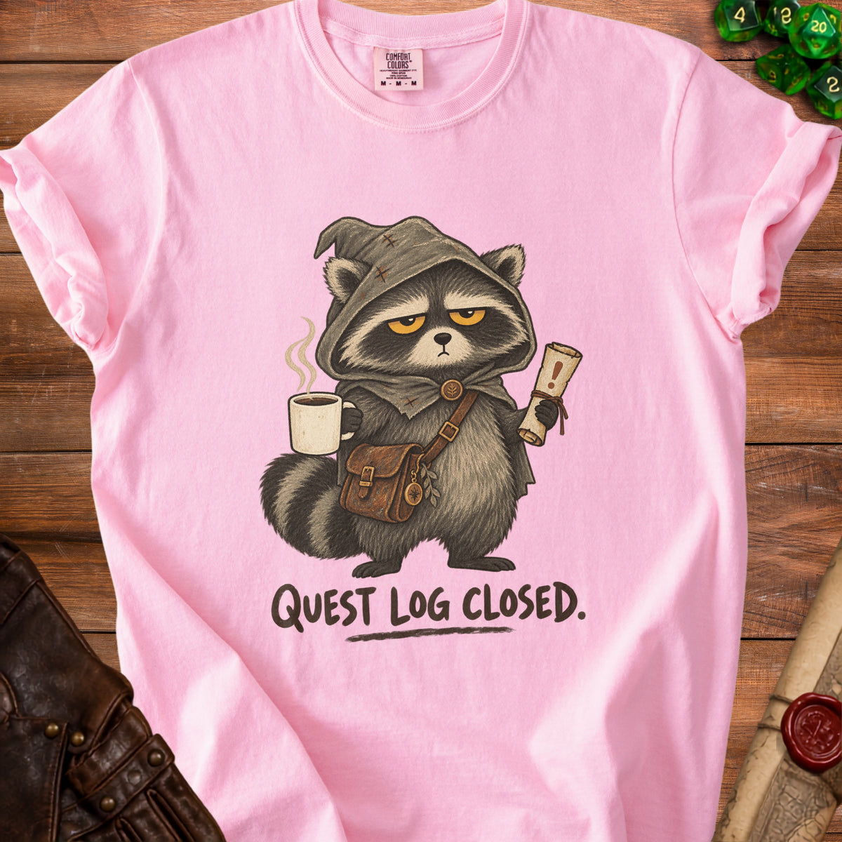 Pink t-shirt with raccoon character in medieval garb holding coffee and scroll, text "QUEST LOG CLOSED."
