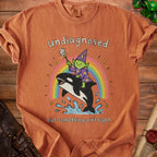Orange t-shirt graphic: wizard riding orca on rainbow, text "undiagnosed but something ain't right".