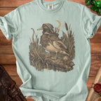A mallard duck dressed as an archer stands on a log near cattails and a river.