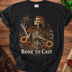 Skeleton in hooded robe holds book surrounded by flowers and dice, "Bone to Cast" text.