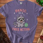 Purple t-shirt with raccoon graphic saying "PANIC IS A FREE ACTION" and a D20 die.