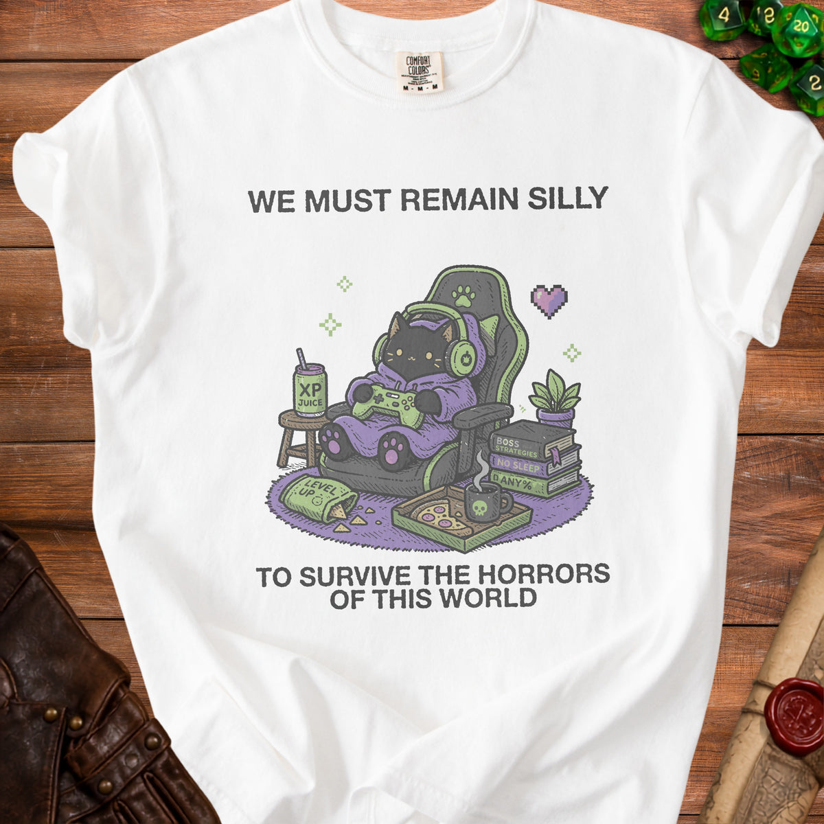 White t-shirt with graphic of a black cat gaming, holding controller, with text "We Must Remain Silly To Survive The Horrors Of This World."