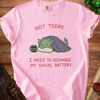 Pink t-shirt with a cartoon dragon resting under a blanket, text reads "NOT TODAY. I NEED TO RECHARGE MY SOCIAL BATTERY."