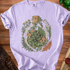 Light purple t-shirt with a glass bottle containing a d20 die, mushrooms, and plants.