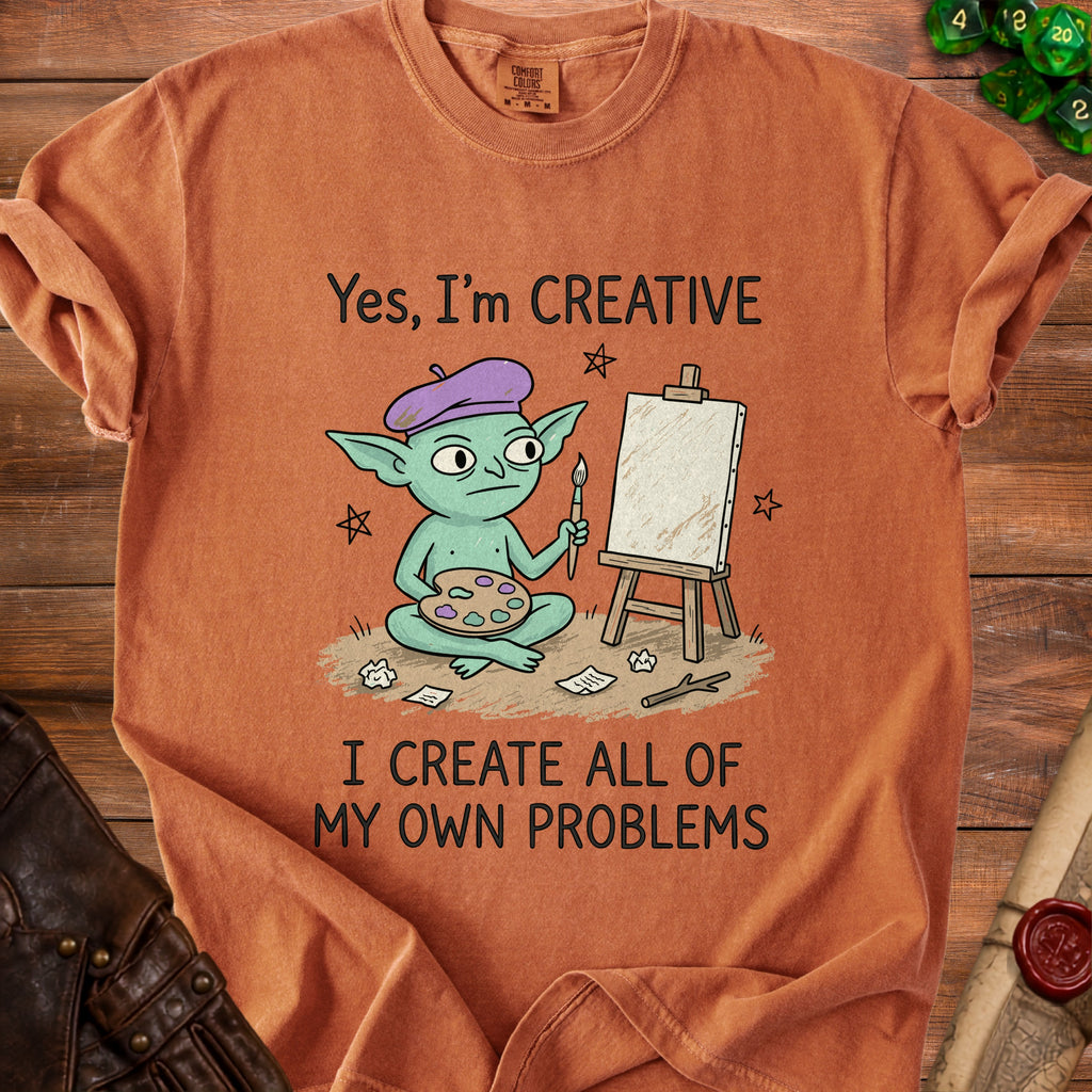 Orange t-shirt with a graphic of a green goblin artist and text: "Yes, I'm CREATIVE I CREATE ALL OF MY OWN PROBLEMS".