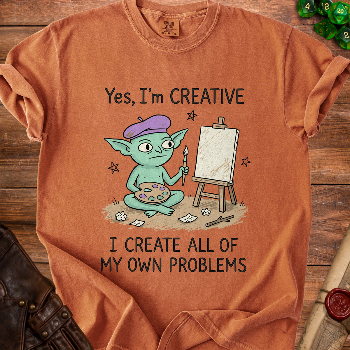 Orange t-shirt with a graphic of a green goblin artist and text: "Yes, I'm CREATIVE I CREATE ALL OF MY OWN PROBLEMS".