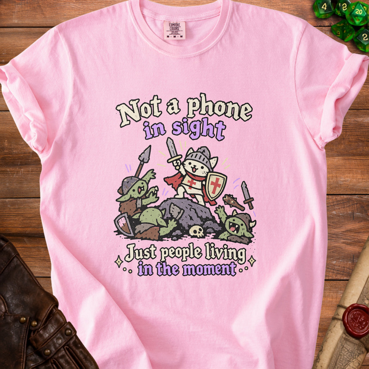 Pink t-shirt with knight cat battling goblins, text reads "Not a phone in sight, Just people living in the moment."