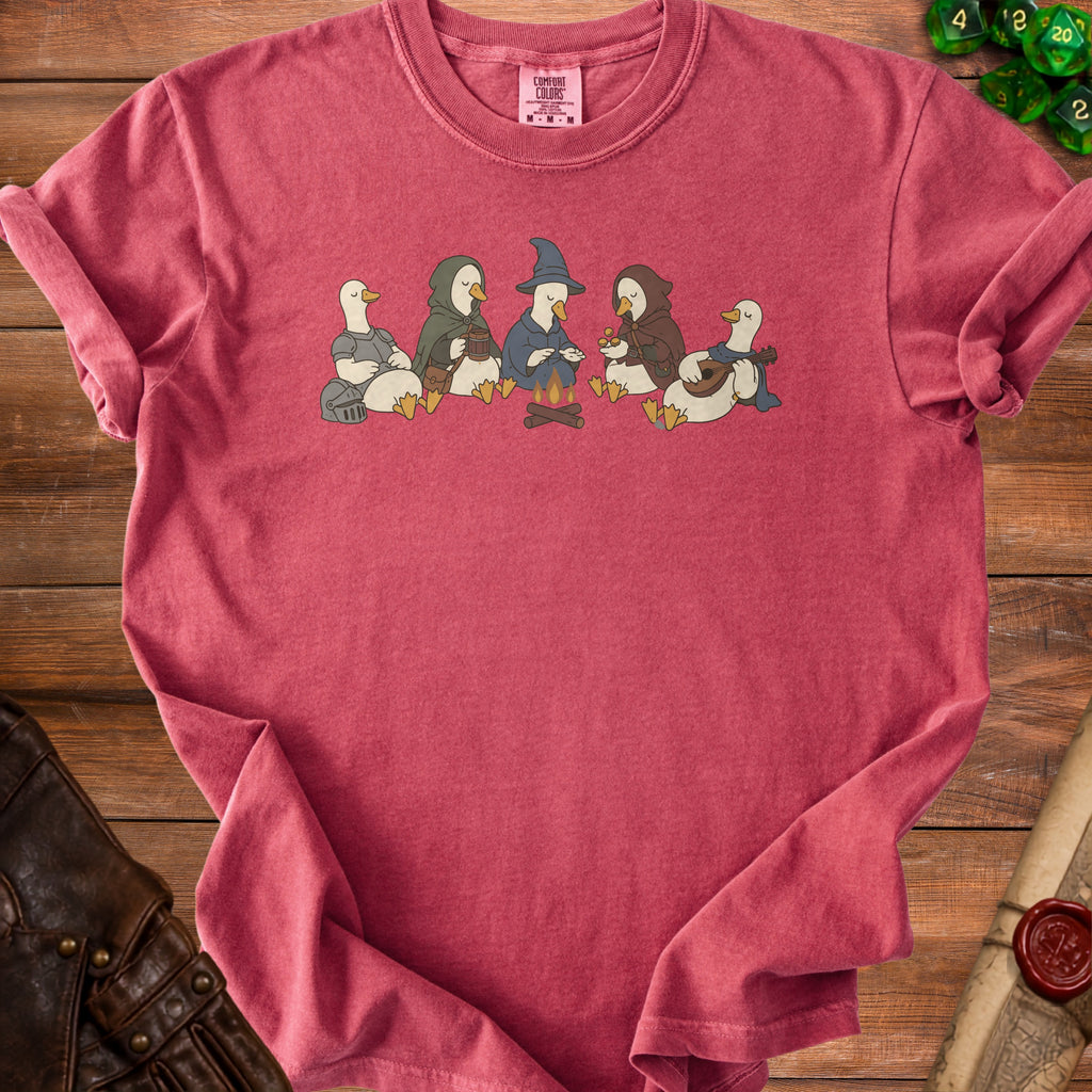 Duck characters in adventuring clothes sit around a campfire on a red t-shirt.