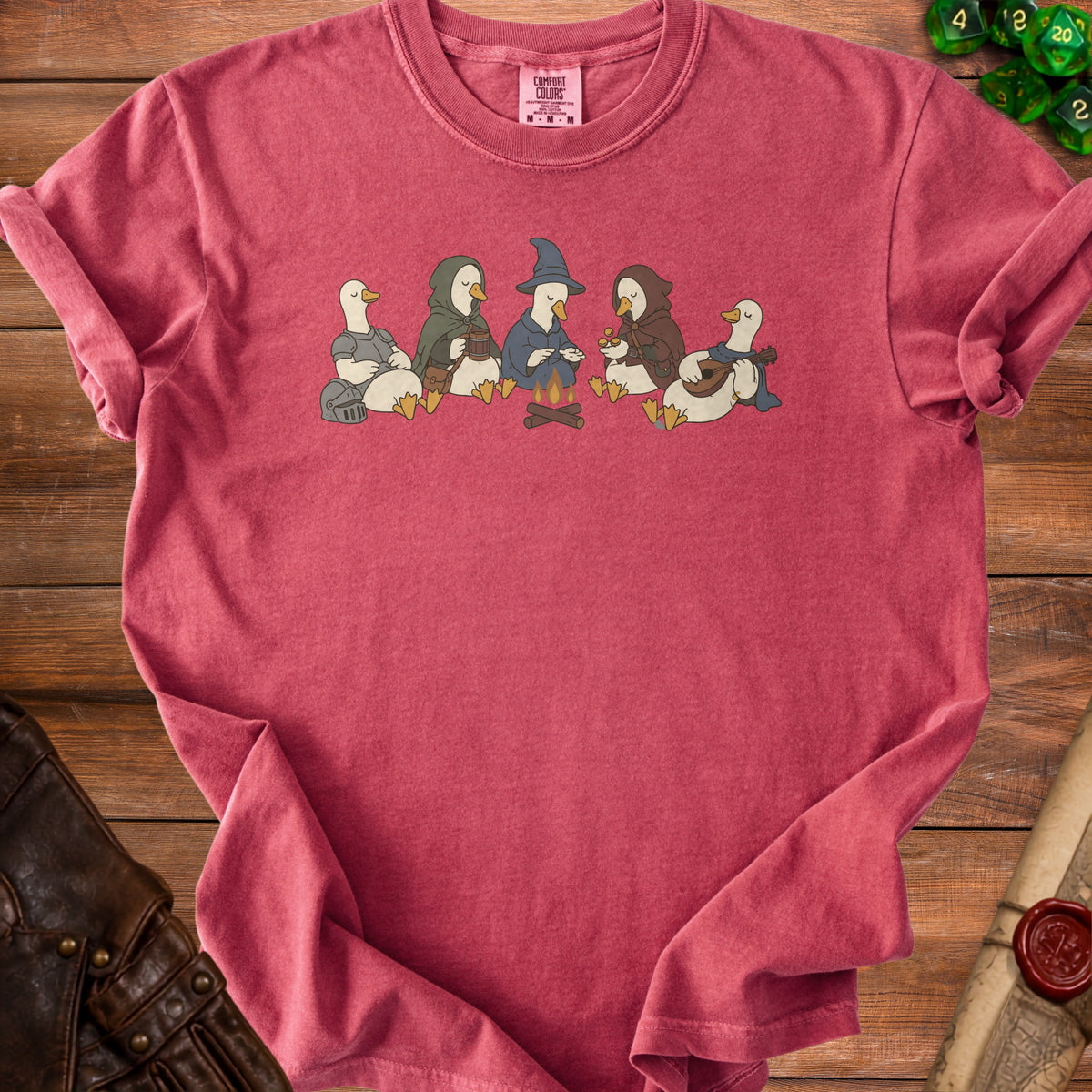 Duck characters in adventuring clothes sit around a campfire on a red t-shirt.