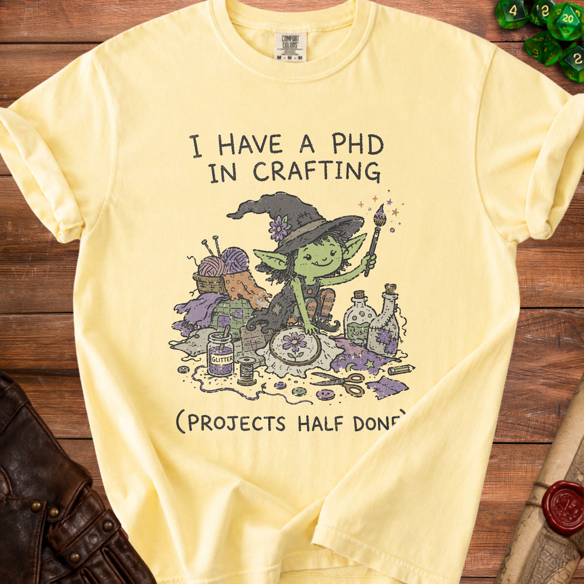 Yellow t-shirt with a graphic of a witch surrounded by crafting supplies and text.