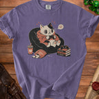 Cat character in hoodie gaming with controller, snacks, and books on purple shirt.