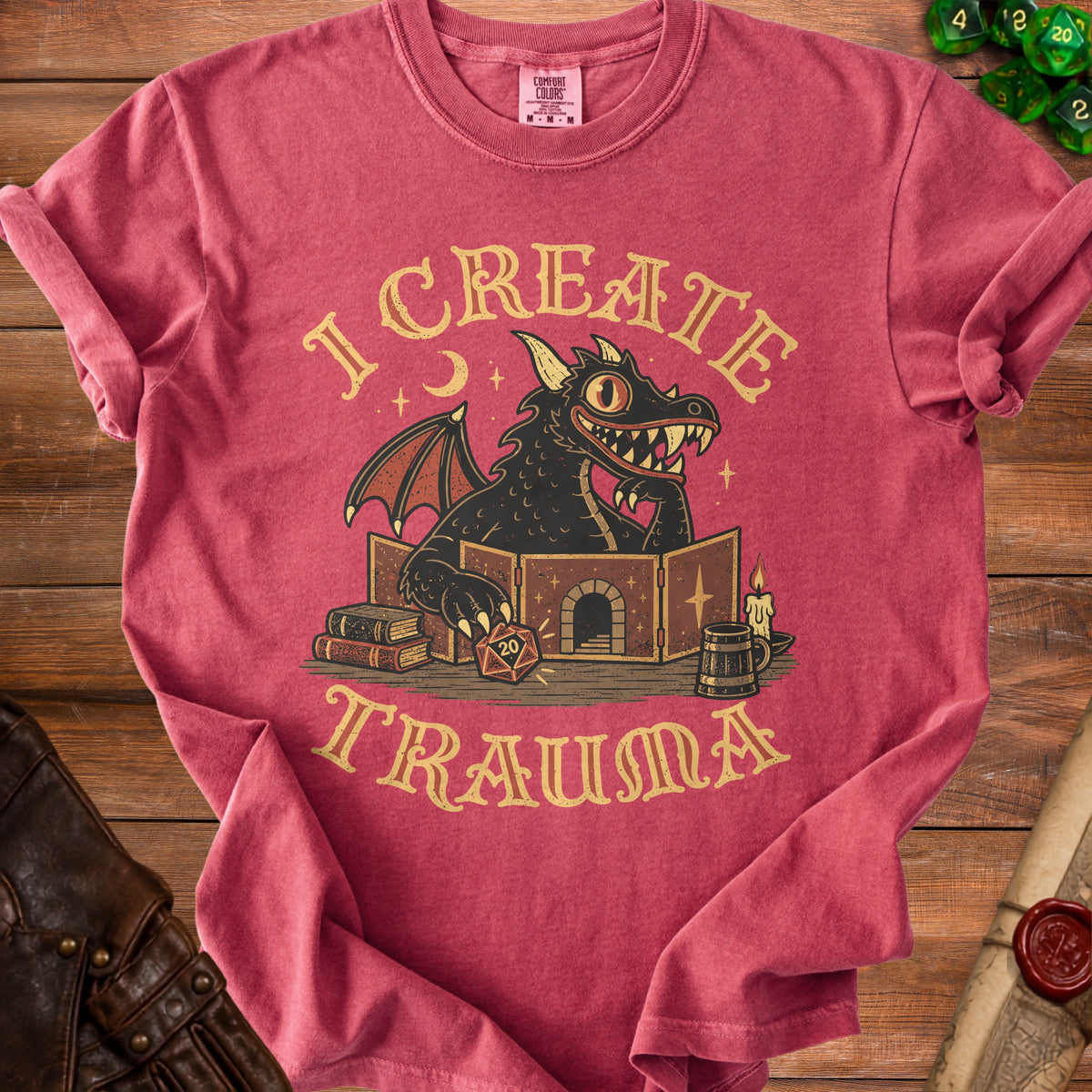 Red t-shirt with a vintage graphic of a black dragon behind a dungeon master screen, featuring the text I CREATE TRAUMA.