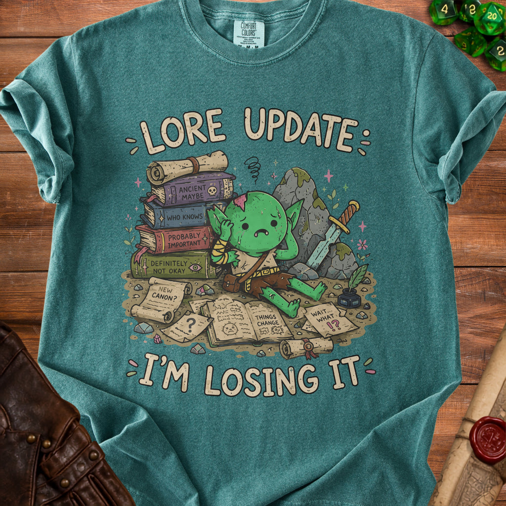 T-shirt graphic of a stressed goblin surrounded by books and scrolls reading "Lore Update I'm Losing It".