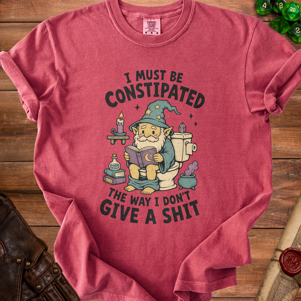 T-shirt with cartoon wizard on toilet reading book, text "I MUST BE CONSTIPATED THE WAY I DON'T GIVE A SHIT".