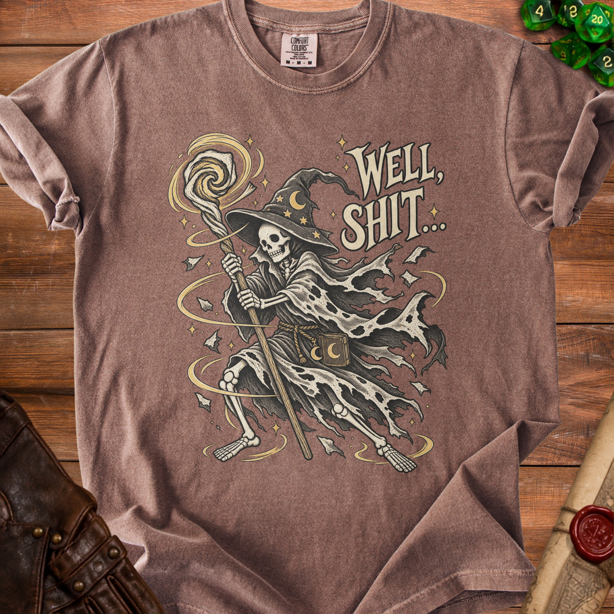 Skeleton wizard graphic with text "WELL, SHIT..." on a brown t-shirt.