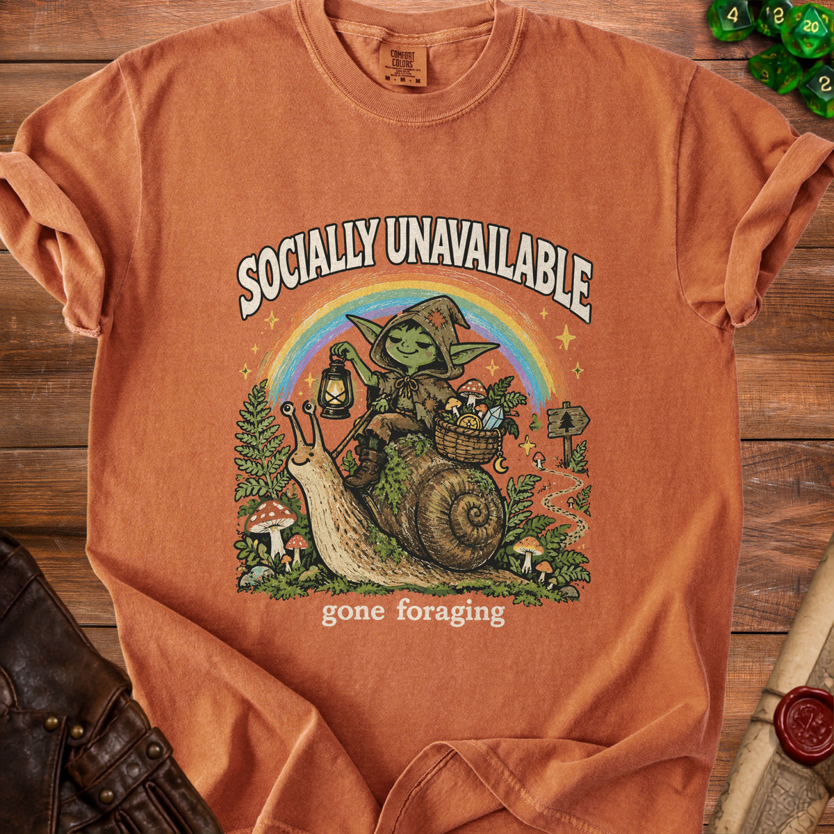 T-shirt with graphic of goblin riding a snail under a rainbow, saying "Socially Unavailable gone foraging".