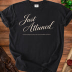 A black t-shirt printed with the beige text Just Attuned and emotionally attached to questionable artifacts.