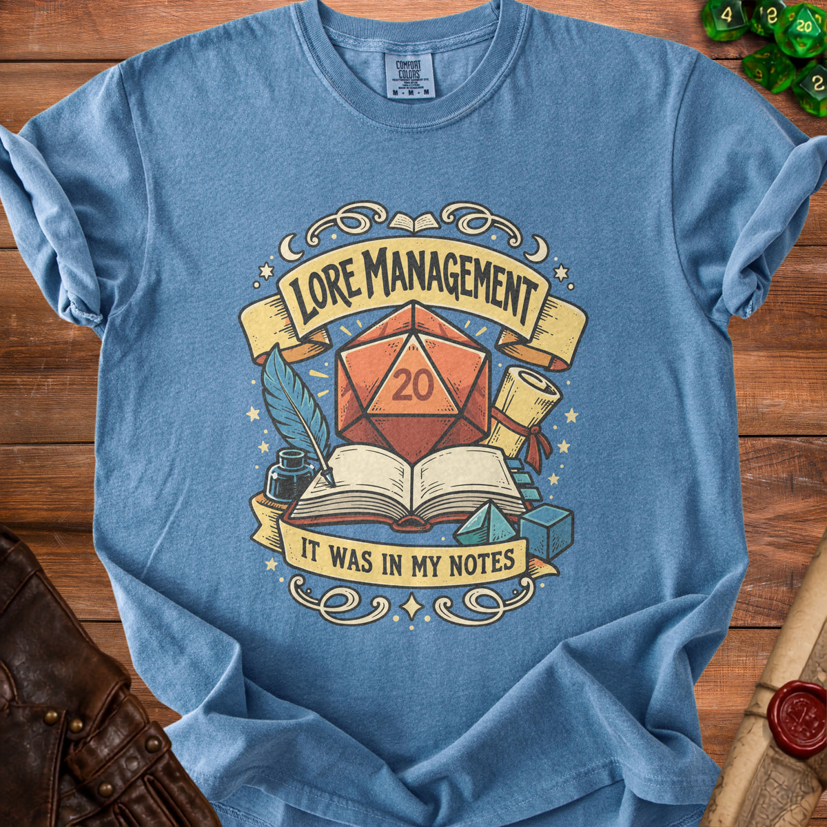 Blue t-shirt with dice, book, quill, and text "LORE MANAGEMENT IT WAS IN MY NOTES".