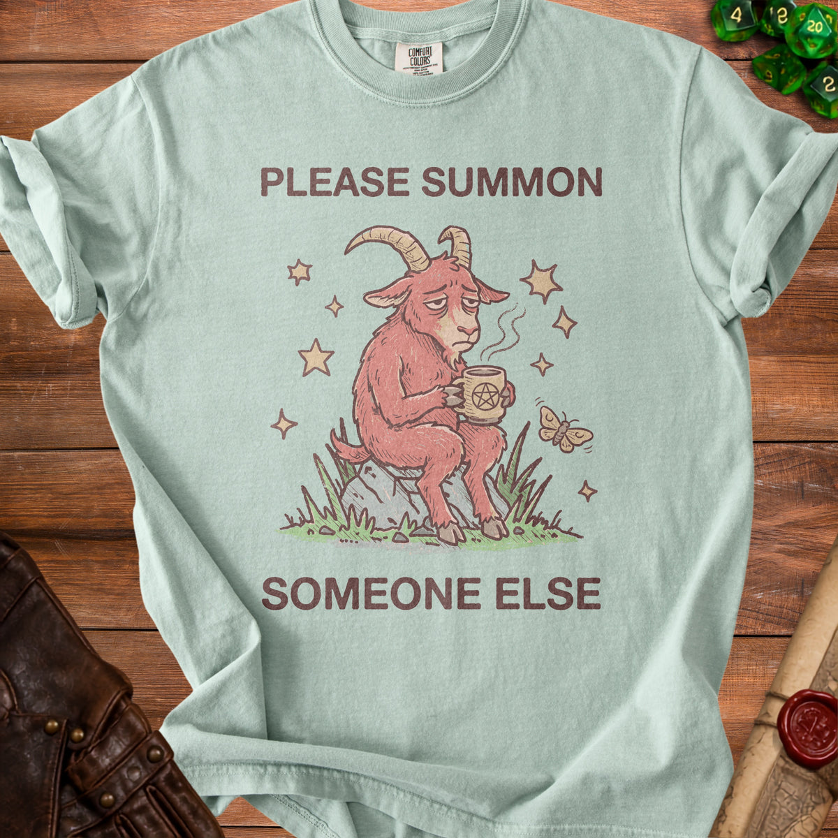 Light blue t-shirt with a drawing of a sad goat holding a pentagram mug.