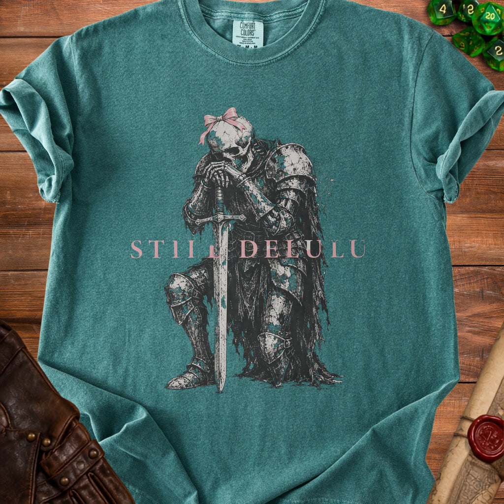 Green t-shirt with a graphic of a skeleton knight with a pink bow and text "STII DELULU".