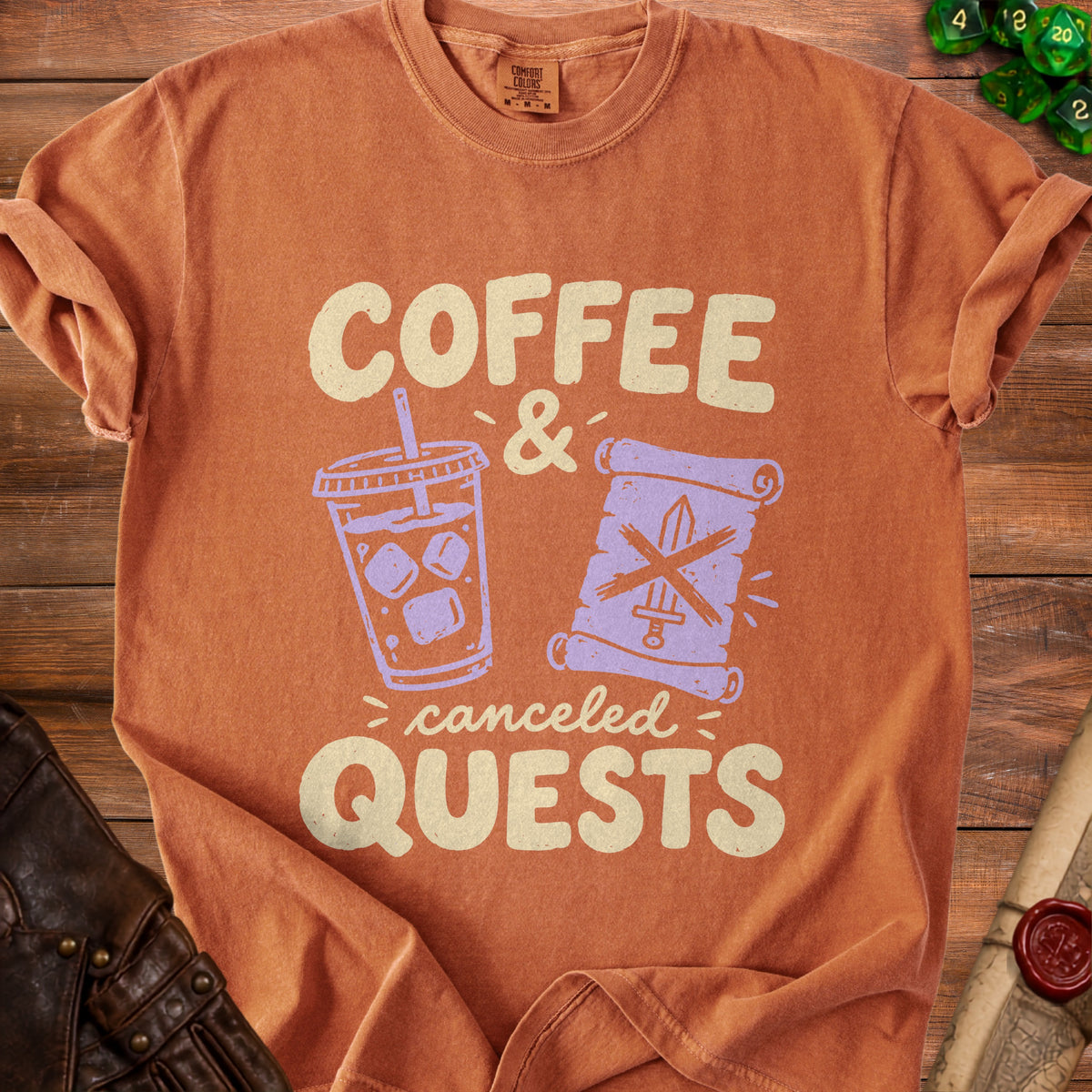 An orange crewneck t-shirt featuring the text COFFEE AND CANCELED QUESTS with a beverage cup and scroll graphic.