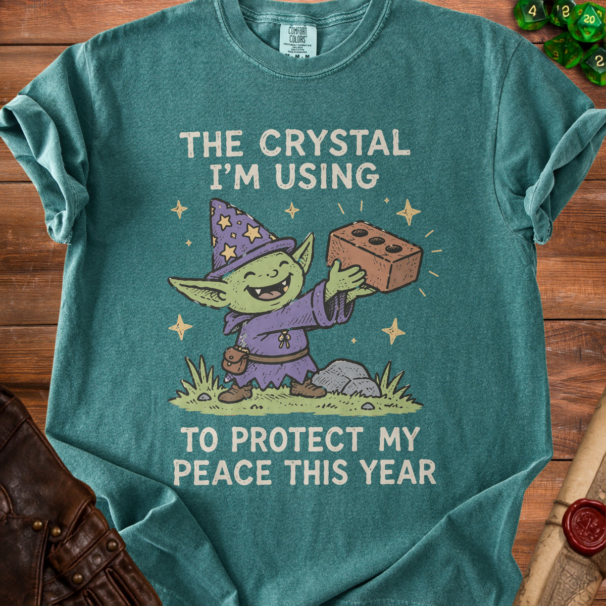 Green t-shirt with goblin wizard holding brick, text "The crystal I'm using to protect my peace this year."