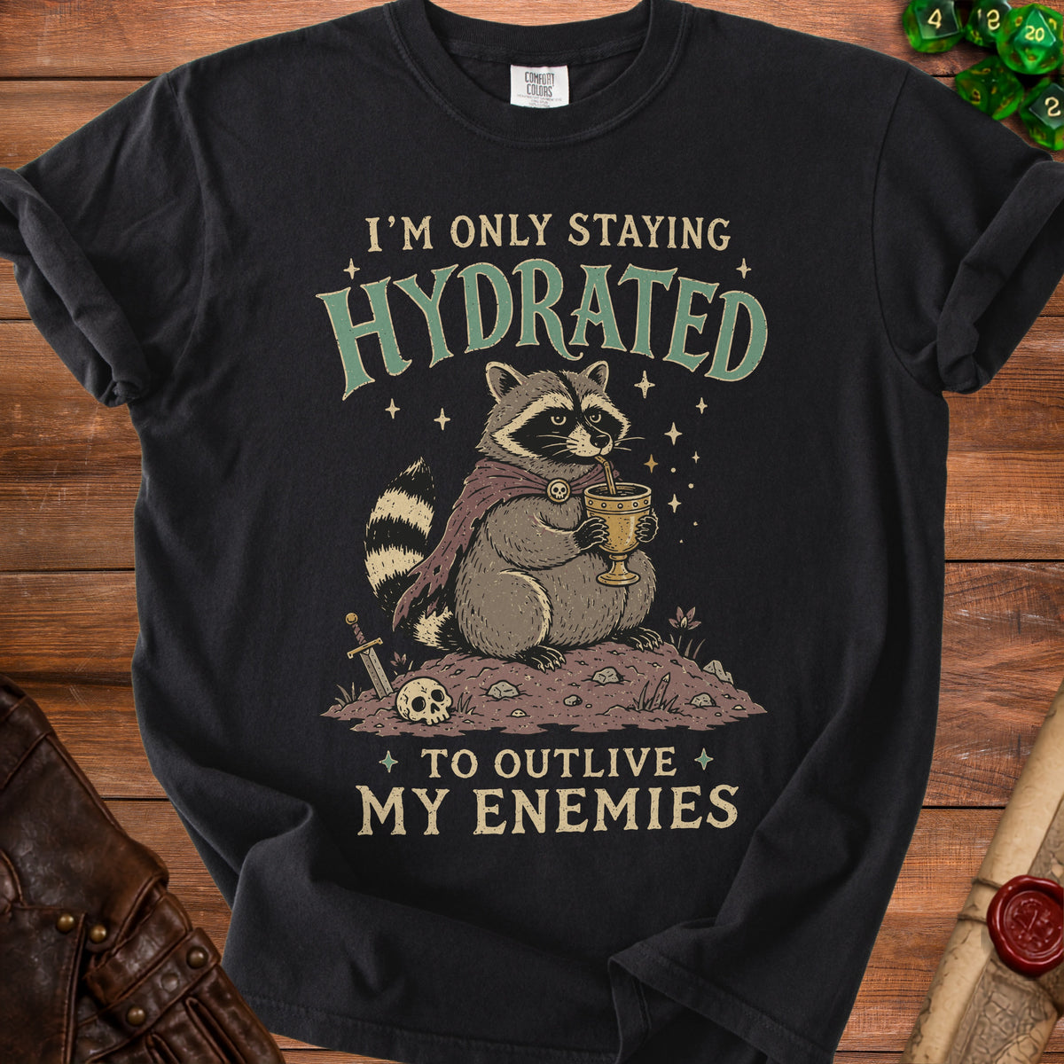 T-shirt with a raccoon drinking from a chalice and the text "I'M ONLY STAYING HYDRATED TO OUTLIVE MY ENEMIES".