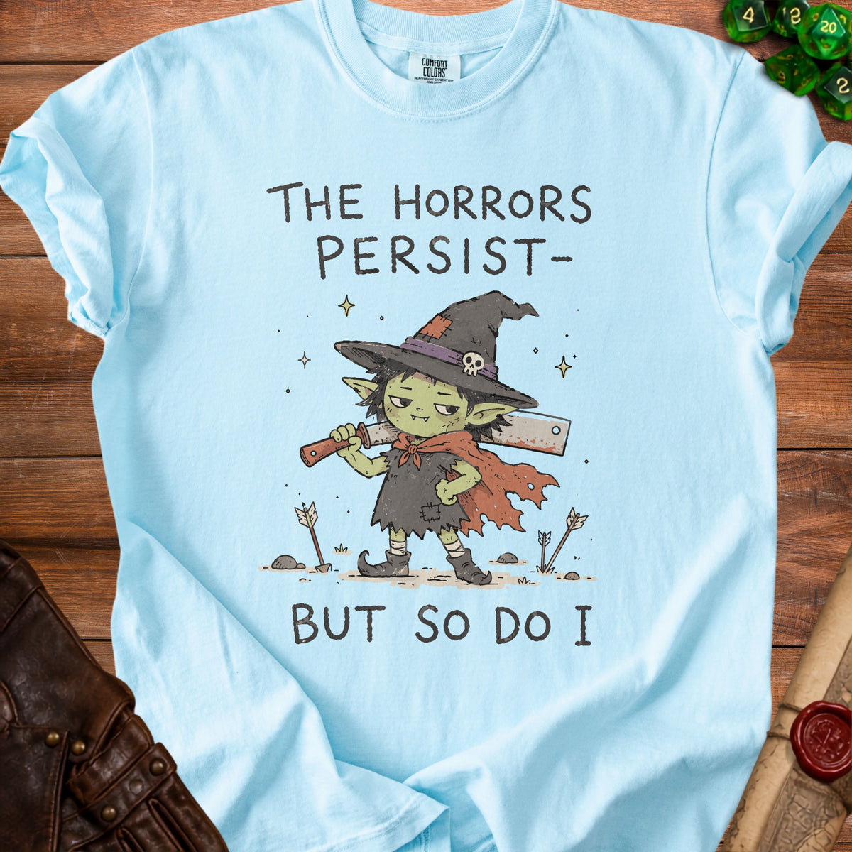 Light blue t-shirt with a goblin character wearing a witch hat and holding a cleaver, text reads "The Horrors Persist- But So Do I".