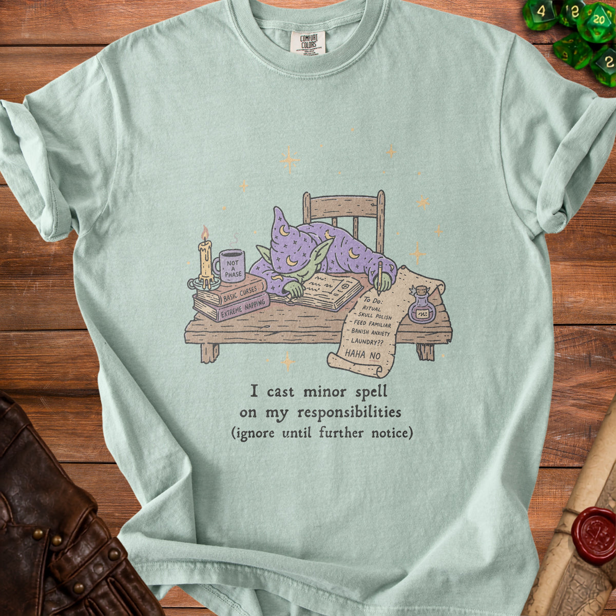 Light blue t-shirt with illustration of a goblin wizard sleeping on books and scroll of tasks.