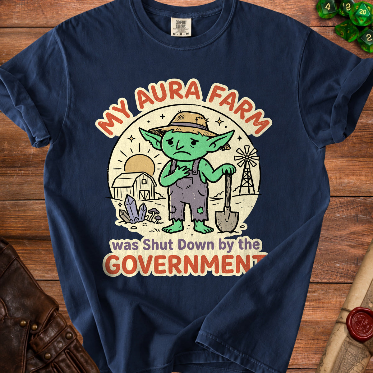 Dark blue t-shirt with a distressed graphic of a sad goblin and farm elements, stating "My Aura Farm was Shut Down by the GOVERNMENT".