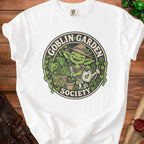 White t-shirt with a "Goblin Garden Society" logo featuring a smiling goblin watering plants.