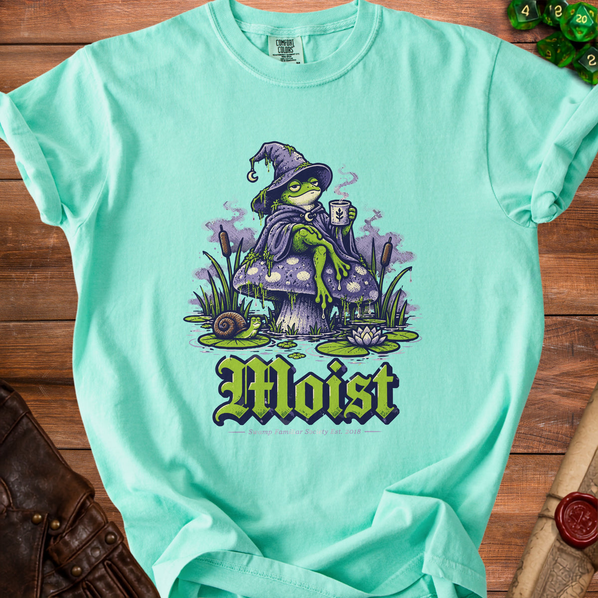 Mint t-shirt with graphic of a frog wizard on a mushroom, text "Moist" and "Swamp Familiar Society Est. 2018".