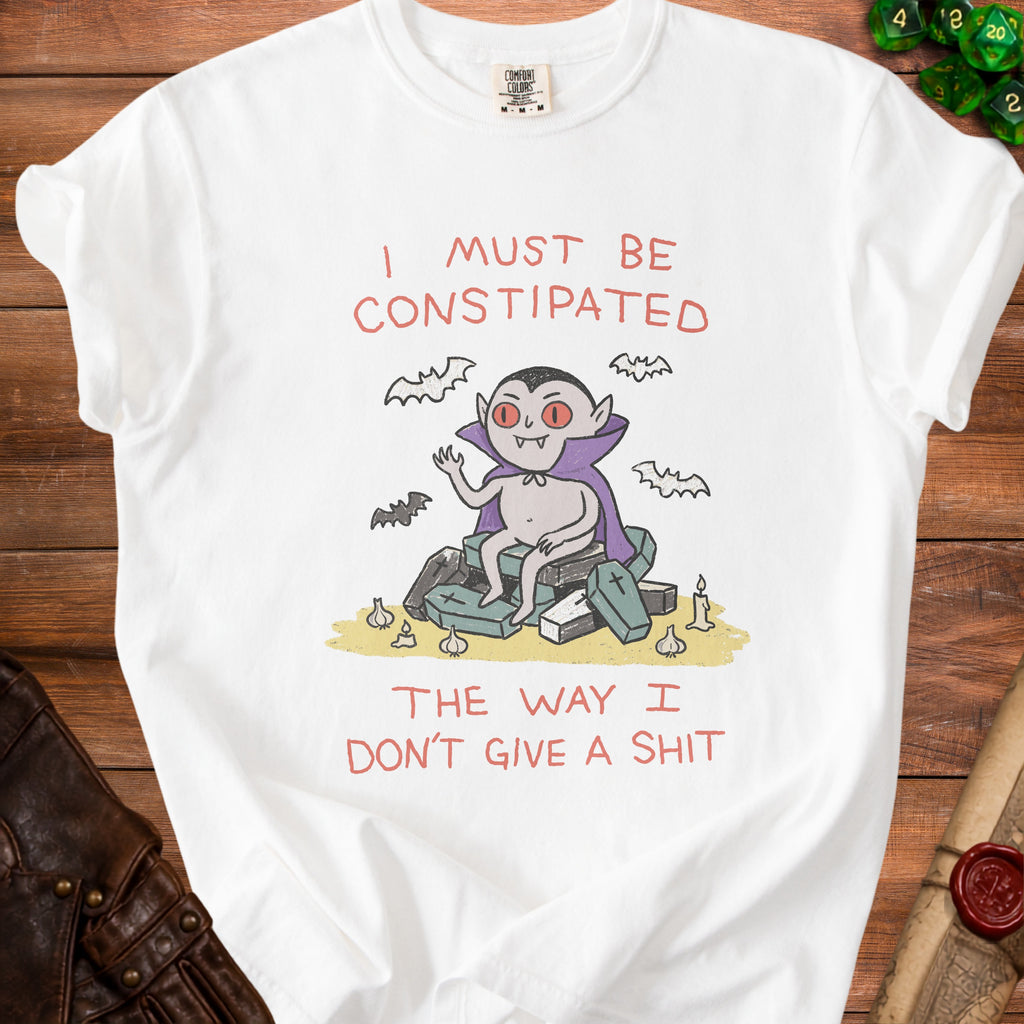White t-shirt with a cartoon vampire on coffins and bats, stating "I must be Constipated The way I Don't Give a Shit".