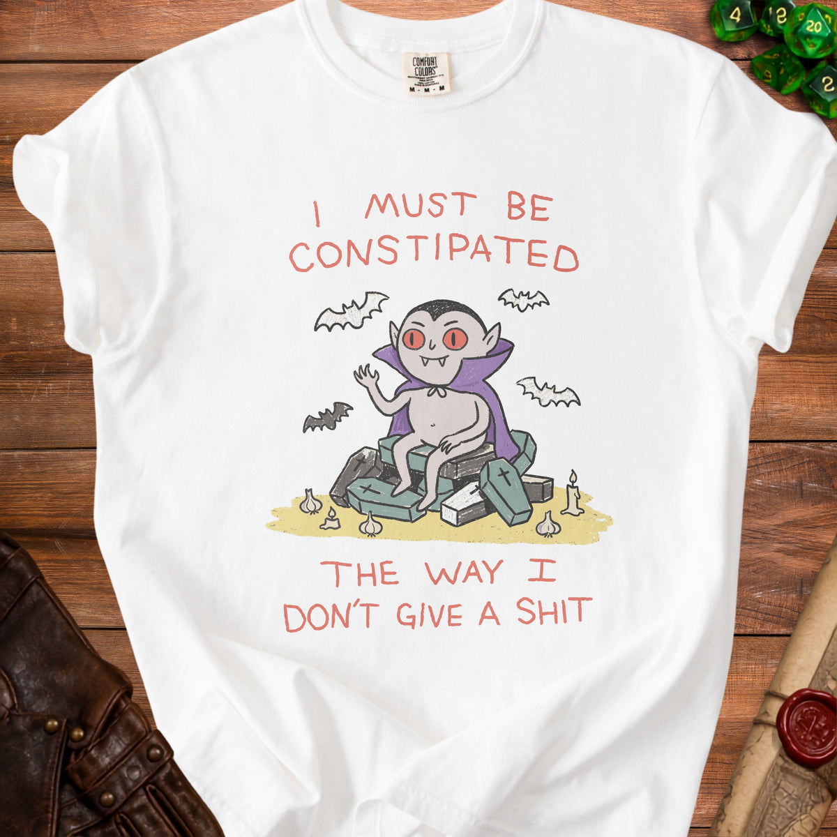 White t-shirt with a cartoon vampire on coffins and bats, stating "I must be Constipated The way I Don't Give a Shit".