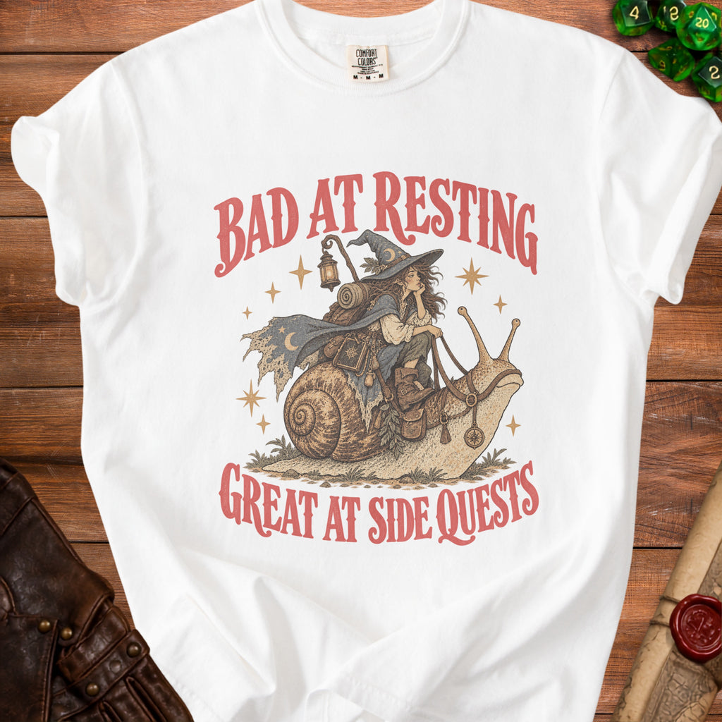 White t-shirt graphic of a witch riding a snail, "Bad at Resting Great at Side Quests".