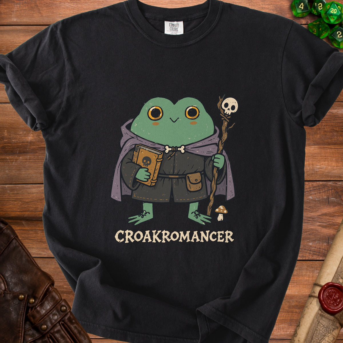 Black t-shirt with a cartoon frog wizard holding a book and staff, text "CROAKROMANCER".
