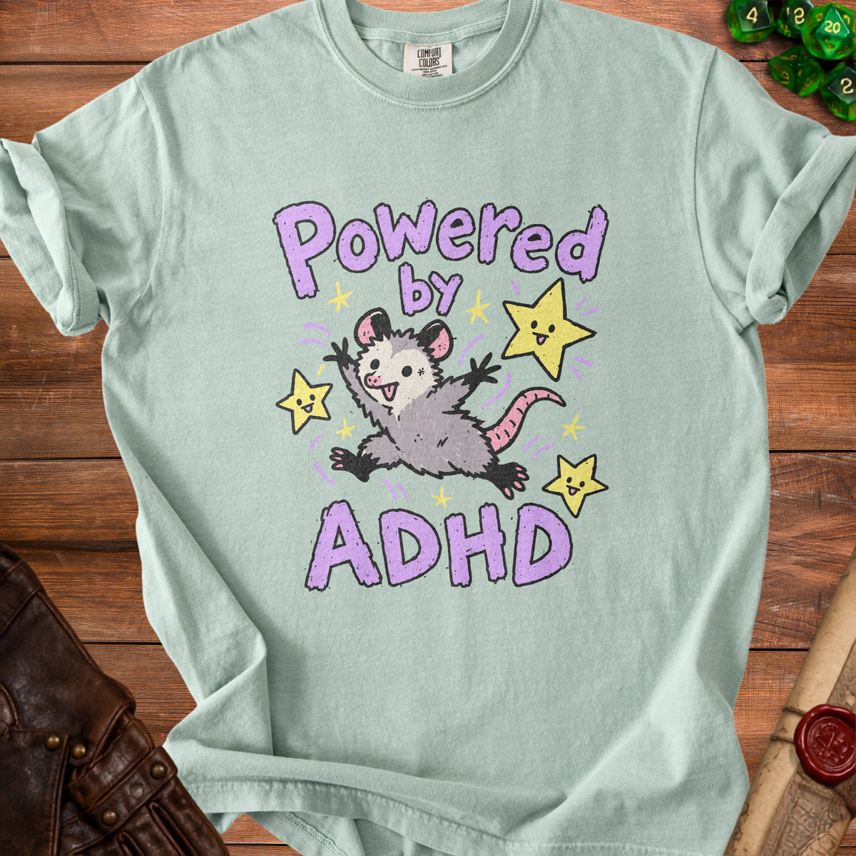 Light green t-shirt with a cartoon possum and stars that says "Powered by ADHD".