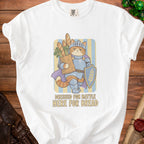 White t-shirt with graphic of knight cat holding baguettes and shield, text "DRESSED FOR BATTLE HERE FOR BREAD".