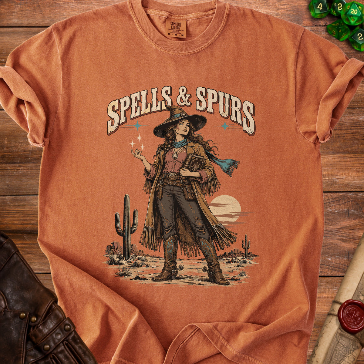 T-shirt with "Spells & Spurs" graphic of a woman in western witch attire in desert.
