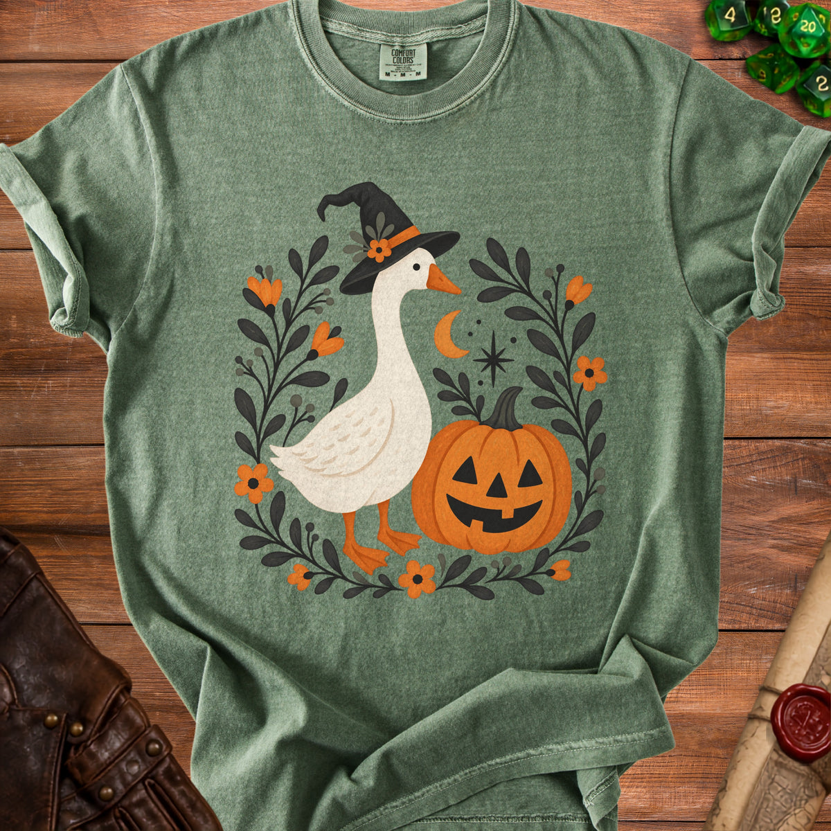 Green t-shirt with a goose wearing a witch hat next to a pumpkin.